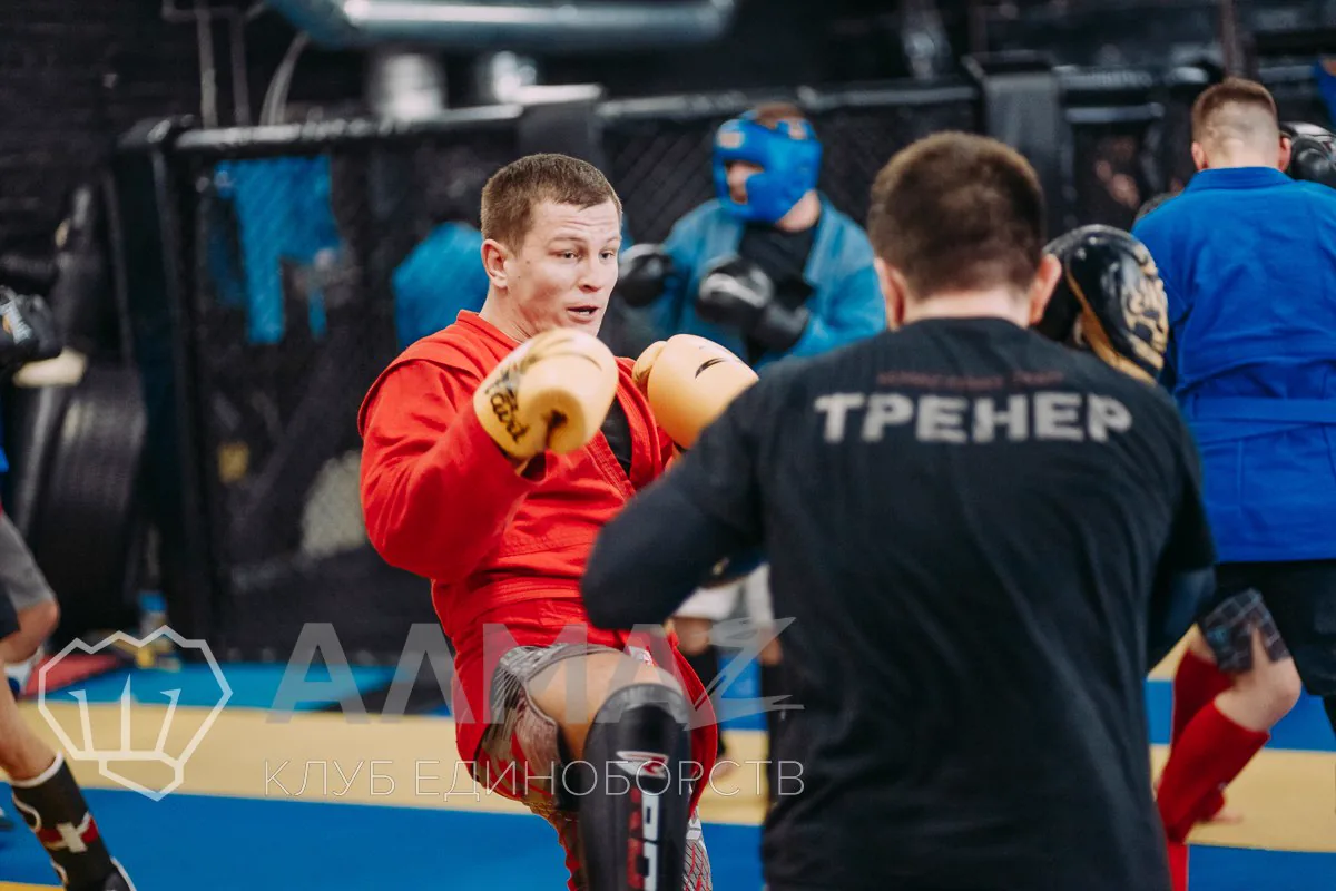 Работа один на один: тренер в футболке с надписью «Тренер» держит лапы, боец в красной самбовке бьёт коленом